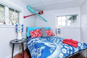 Ein Schlafzimmer mit Bett, Fenster, Lampe und einem an der Wand befestigten Surfbrett.