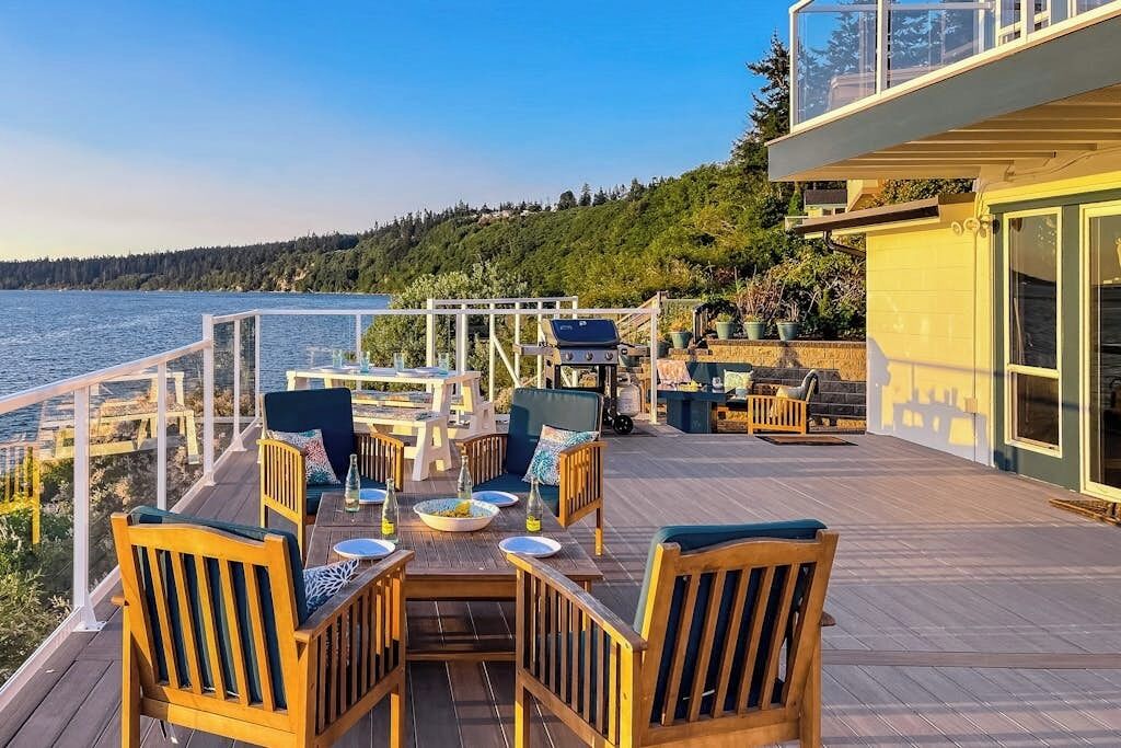 A deck with outdoor furniture, a grill, and a view of the water.