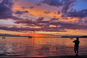 Tramonto su una superficie d'acqua calma con una persona che pesca.