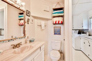 Un bagno con uno specchio grande, un lavandino, un water e un angolo lavanderia con cesti per la biancheria impilati.