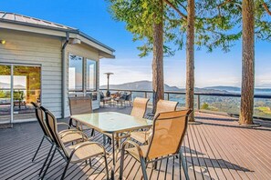A deck with a table and chairs, overlooking a scenic landscape. - Stunning Mountaintop Retreat with Private Sauna and Water Views (Eastsound)