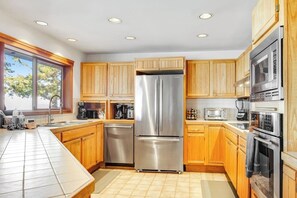 Een moderne keuken met houten kasten, roestvrijstalen apparatuur en een groot raam voor natuurlijk licht.