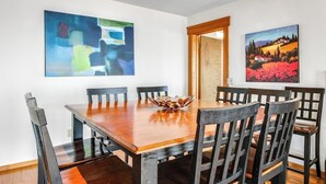 A dining area with a wooden table and chairs, a bowl centerpiece, and two paintings on the walls. - Stunning Mountaintop Retreat with Private Sauna and Water Views (Eastsound)
