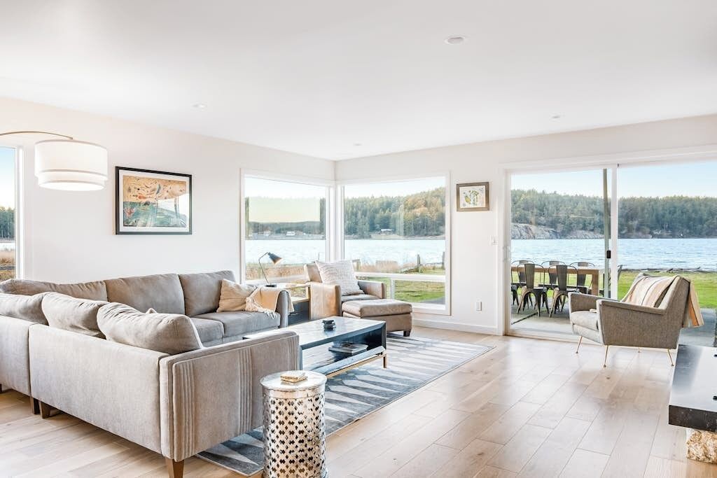 A spacious living room with a large sofa, a coffee table, and a view of a lake.