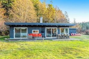 A modern house with a covered patio, a red sofa, and a dining area. - Accessible Waterfront Holiday Home with Bay Views and Family Friendly Features (Lopez Island)