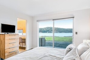 A bedroom with a bed, a television on a dresser, a desk, and a view of a lake through a sliding glass door. - Accessible Waterfront Holiday Home with Bay Views and Family Friendly Features (Lopez Island)