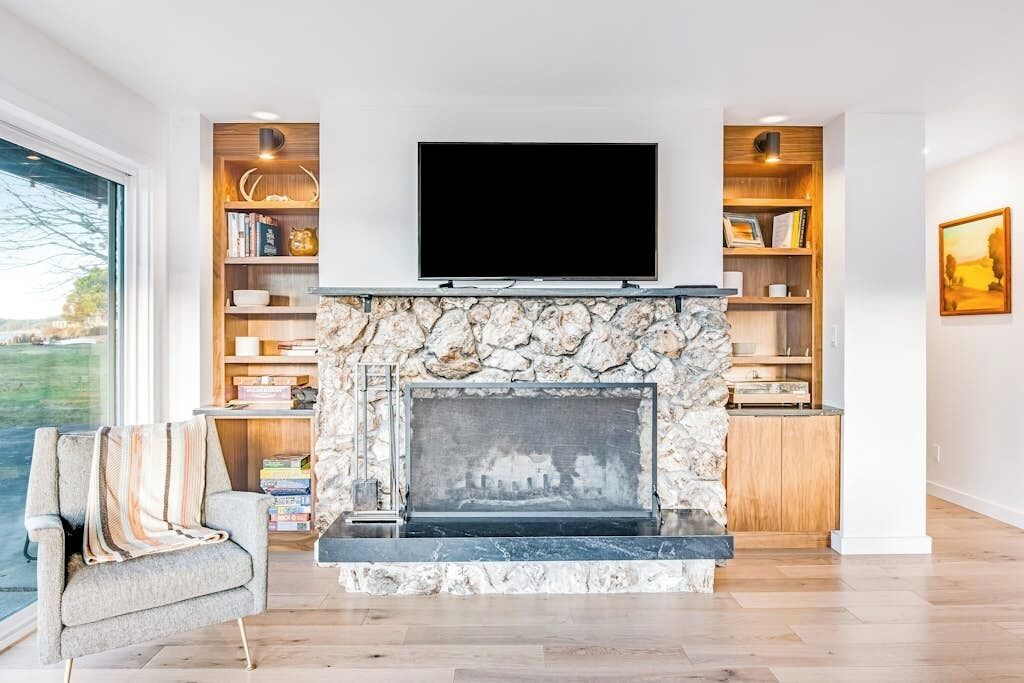 A living room with a stone fireplace, a flat-screen TV mounted above it, and bookshelves on either side.