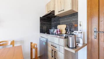 Cocina compacta con armarios de madera, estufa integrada, cafetera y hervidor.