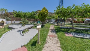 A paved pathway with a green signpost, surrounded by grass and trees, leading to a building with a sloped roof. - Family Beachfront Apartment with Sea View in Agia Galini, Crete (Agia Galini)