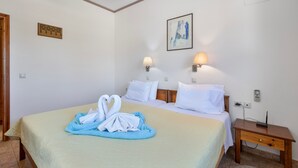 A hotel room with a bed, two bedside lamps, a painting on the wall, and a wooden nightstand with a phone. - Family Beachfront Apartment with Sea View in Agia Galini, Crete (Agia Galini)