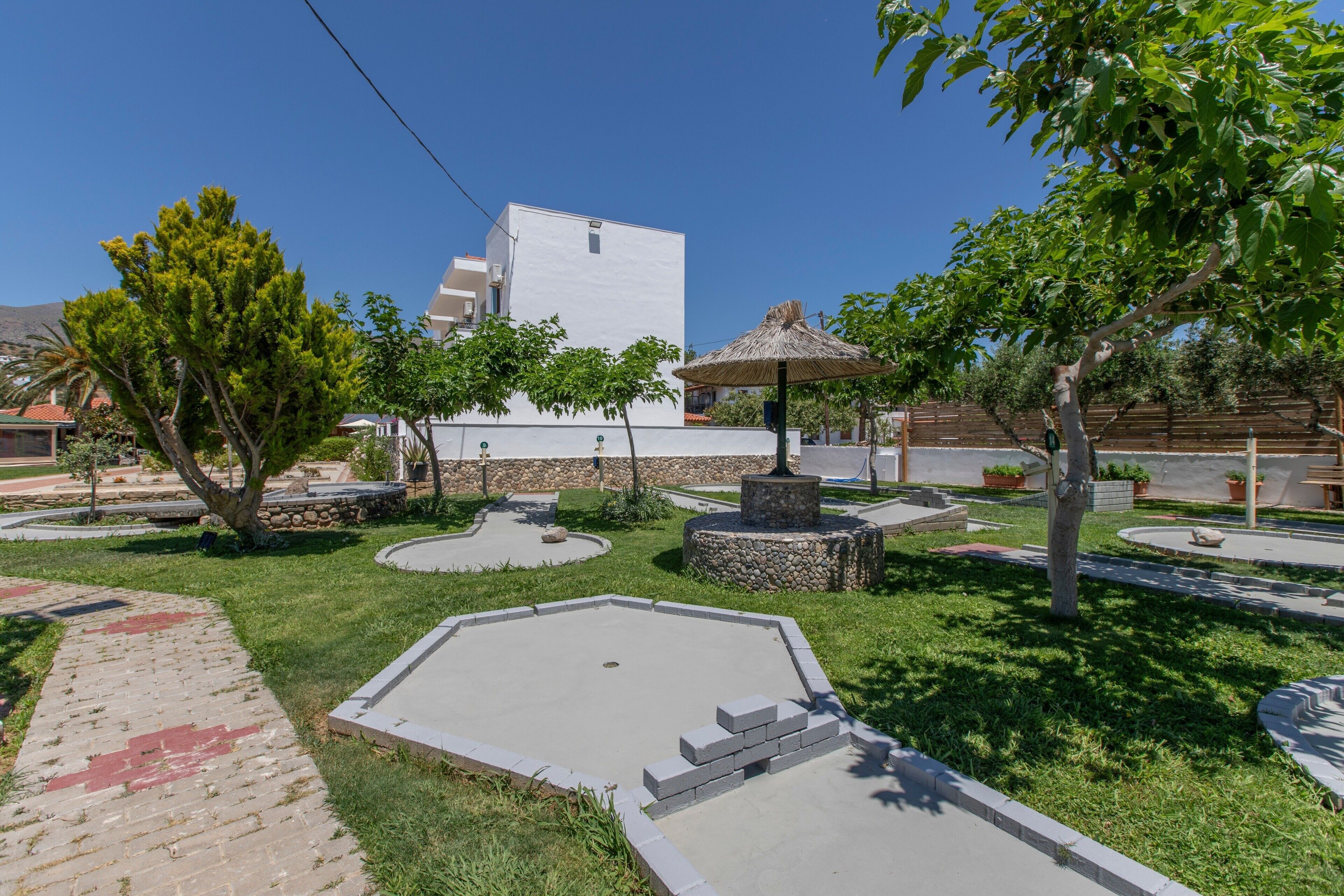 Un patio ajardinado con un edificio blanco, una fuente de piedra y un paraguas de paja.
