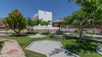 Un patio ajardinado con un edificio blanco, una fuente de piedra y un paraguas de paja.