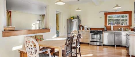 A kitchen with a dining table, chairs, a refrigerator, an oven, and a window.