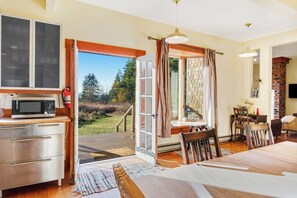 Una habitación con mesa de comedor, sillas, una zona de cocina con microondas y un ventanal con cortinas.