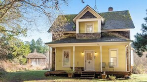 A two-story house with a porch, a front door, and a chimney. - Classic farmhouse-style home with front porch & amazing sunset views - walk to town (Lopez Island)