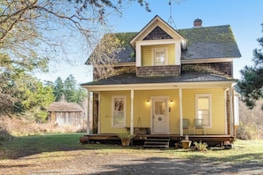 A two-story house with a porch, a front door, and a chimney. - Classic farmhouse-style home with front porch & amazing sunset views - walk to town (Lopez Island)