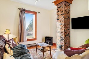 Una sala de estar con chimenea de ladrillo, un sofá, una mesa y un televisor montado en la pared.