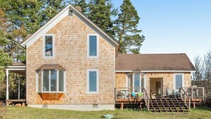 A two-story house with a covered porch, a deck, and a small outdoor seating area. - Classic farmhouse-style home with front porch & amazing sunset views - walk to town (Lopez Island)