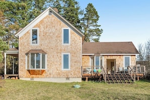 A two-story house with a covered porch, a deck, and a small outdoor seating area. - Classic farmhouse-style home with front porch & amazing sunset views - walk to town (Lopez Island)