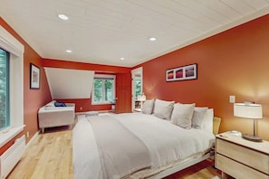 A bedroom with a bed, bedside table, nightstand, and a window with a view of trees. - Renovated 3 Bedroom Eastsound Home with Hot Tub Fire Pit and Stunning Sound Views (Eastsound)