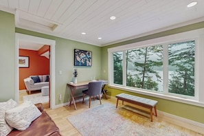 A room with a desk, chair, bench, and a large window with a view of trees. - Renovated 3 Bedroom Eastsound Home with Hot Tub Fire Pit and Stunning Sound Views (Eastsound)