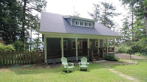 A house with a porch, two chairs, and a grassy yard. - Renovated 3 Bedroom Eastsound Home with Hot Tub Fire Pit and Stunning Sound Views (Eastsound)