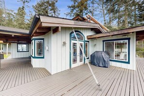 A wooden deck with a covered outdoor seating area and a building with a gabled roof. - Pet Friendly Waterfront Escape with Fire Pit, Hot Tub and Mountain Views on Lopez Island (Lopez Island)