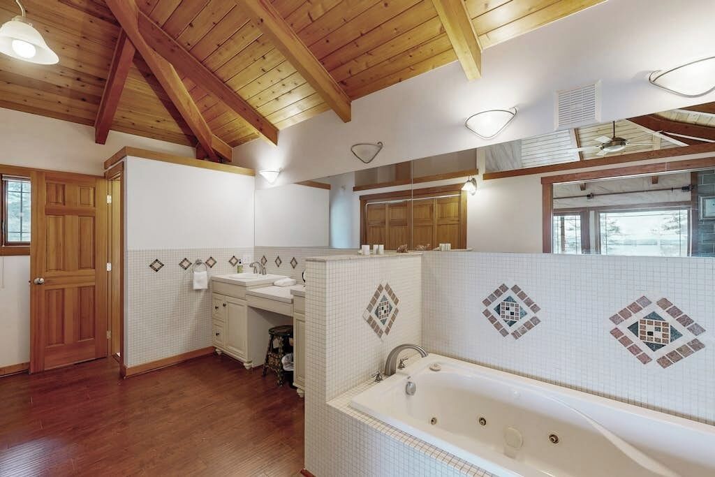 Un baño con techo de madera, paredes de azulejos blancos, una bañera y un tocador con espejo.