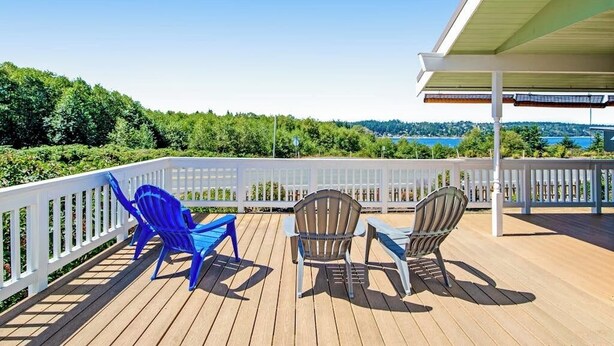 Una terraza de madera con dos sillas Adirondack y barandilla blanca.