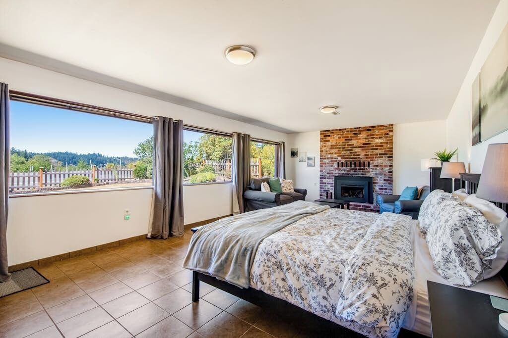 Un dormitorio con una cama grande, una chimenea y un balcón con vistas a un bosque.