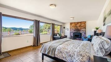 Un dormitorio con una cama grande, una chimenea y un balcón con vistas a un bosque.