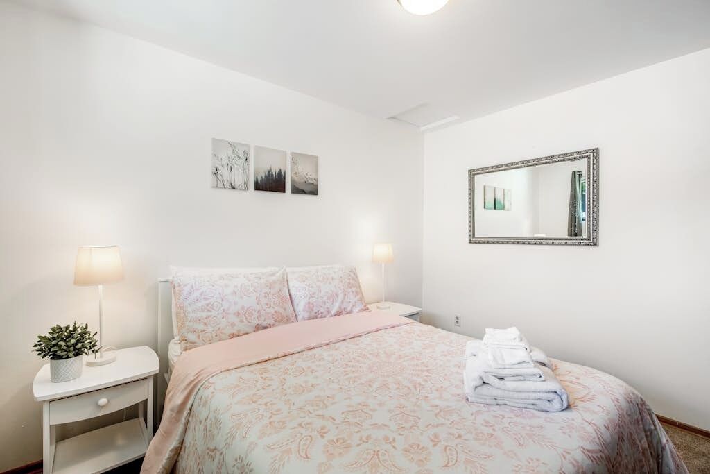A bedroom with a bed, bedside lamps, a mirror, and wall art.