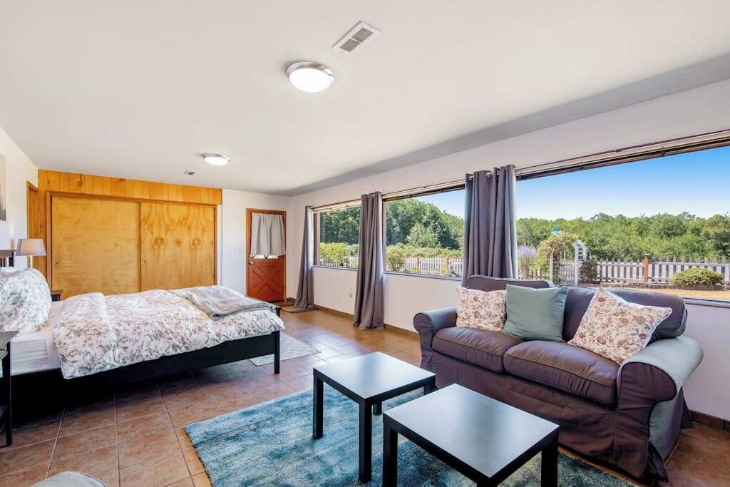 Een slaapkamer met een bed, een bank, een tafel en een groot raam met gordijnen.