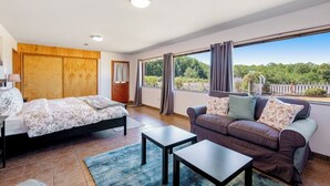 Un dormitorio con cama, sofá, mesa y un ventanal con cortinas.