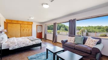 Een slaapkamer met een bed, een bank, een tafel en een groot raam met gordijnen.