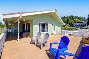 A covered outdoor deck with two Adirondack chairs, a wooden deck, and a light green building with a white roof. - Relaxing Coastal Retreat with Garden and Water Views in Freeland (Freeland)