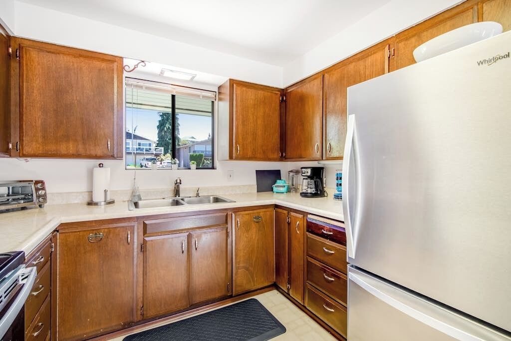 A kitchen with wooden cabinets, a stainless steel refrigerator, and a window with a view of houses.