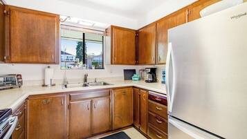 A kitchen with wooden cabinets, a stainless steel refrigerator, and a window with a view of houses.