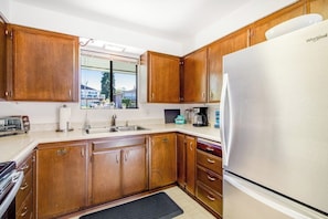Una cocina con armarios de madera, un refrigerador de acero inoxidable y una ventana con vistas a casas.