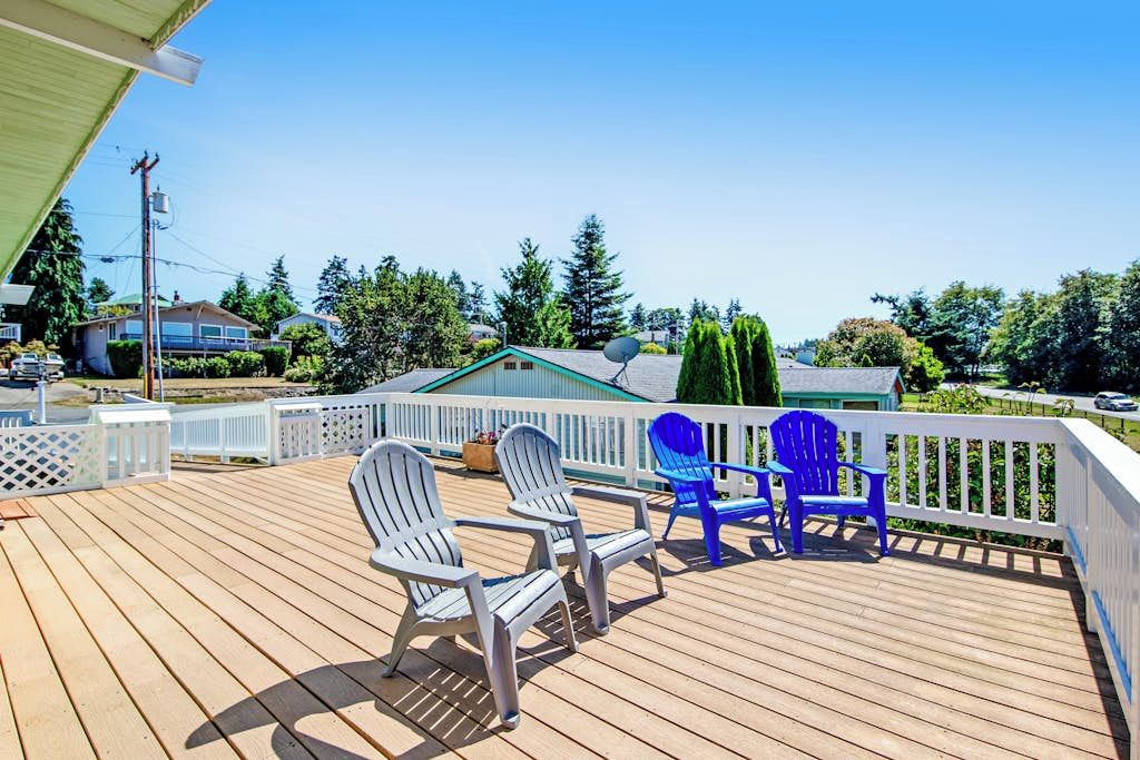 A wooden deck with two Adirondack chairs, one white and one blue, and a white railing.
