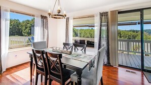 Comedor con mesa, sillas y candelabro. Amplias ventanas con cortinas y vista a zonas verdes.
