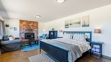 A bedroom with a brick fireplace, a bed with a blue headboard, a grey sofa, and a small table.