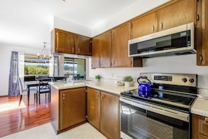 A modern kitchen with wooden cabinets, stainless steel appliances, and a dining area with a view.