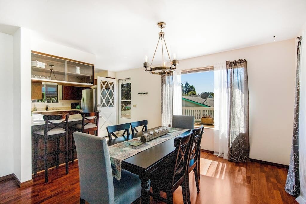 A dining area with a wooden table and chairs, a chandelier, and a view of the outdoors.