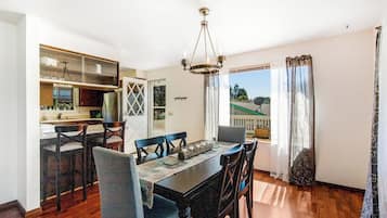 A dining area with a wooden table and chairs, a chandelier, and a view of the outdoors.