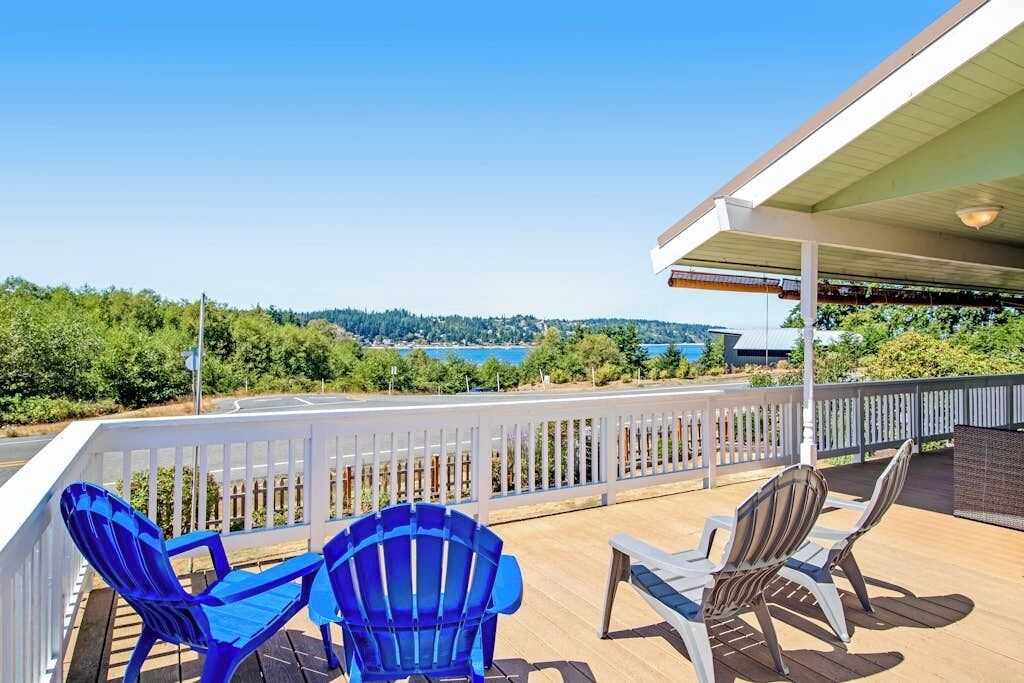 A deck with outdoor seating, a view of a body of water, and a white fence.