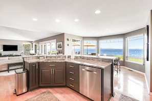 Una cocina moderna con una isla grande, muebles oscuros y vistas al mar.