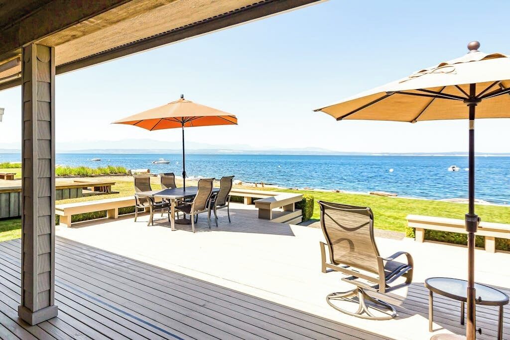 Eine Terrassensitzgelegenheit im Freien mit Blick auf das Meer, ausgestattet mit Tischen und Stühlen unter Sonnenschirmen.