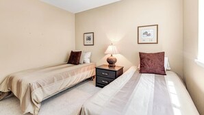 Een hotelkamer met twee éénpersoonsbedden, een nachtkastje met een lamp en twee ingelijste foto's aan de muur.