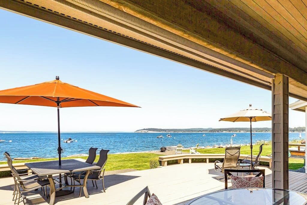 Eine Terrasse im Freien mit Meerblick, ausgestattet mit einem Tisch und Stühlen unter einem Sonnensegel.